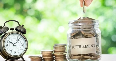 Hand putting Coins in glass jar with retro alarm clock , retirement